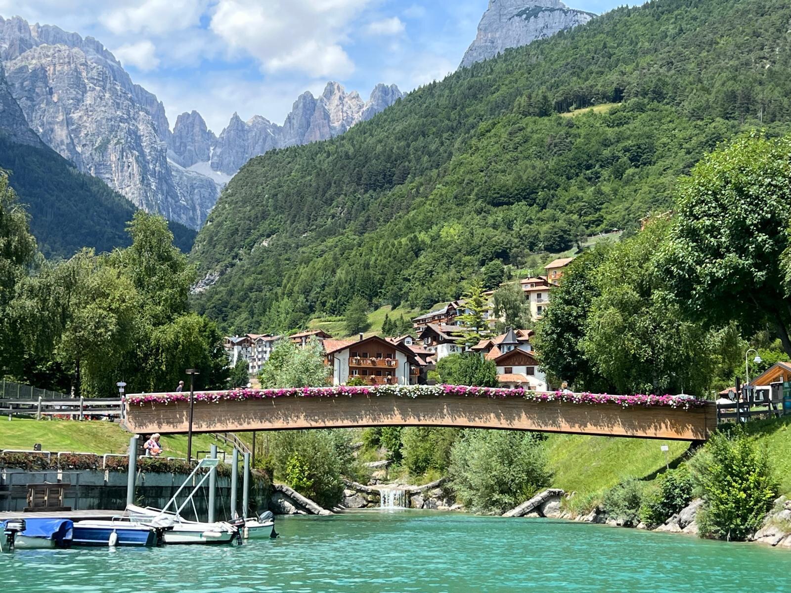 A flower-lined bridge over a turquoise lake beneath the Dolomites in northern Italy